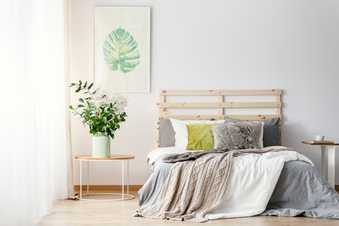 Real photo of a bed with grey and white bedding between two small tables in minimal bedroom interior with a poster on a wall